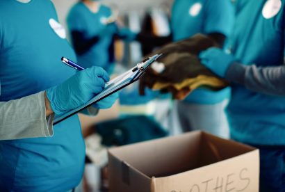 Close-up of woman taking notes while volunteers are packing donation boxes for charity.